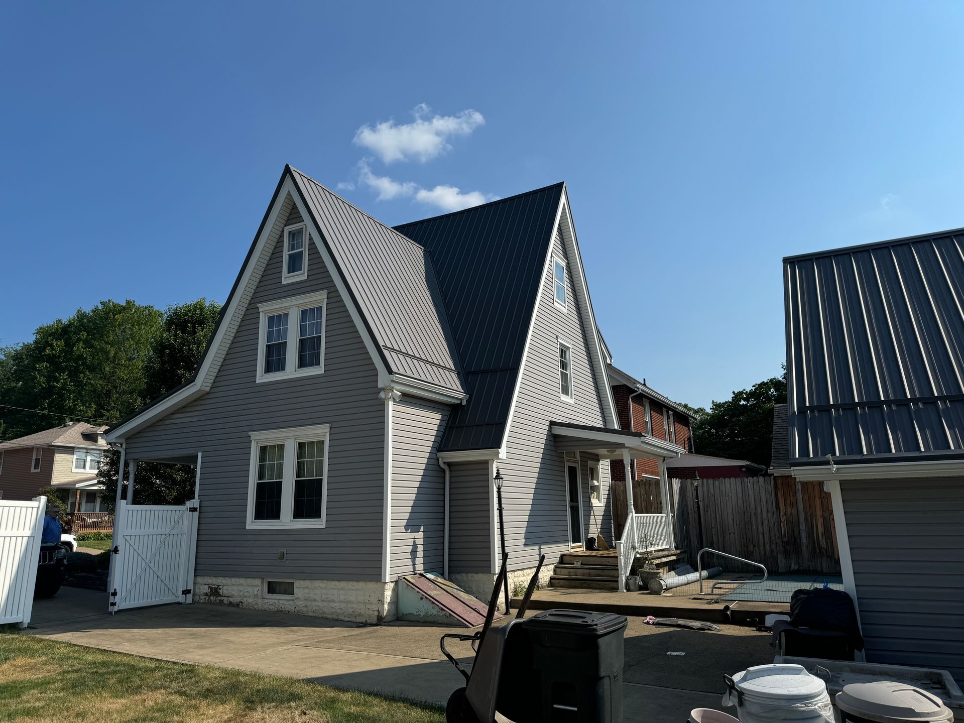 A gray house with a black roof is sitting on top of a lush green field.