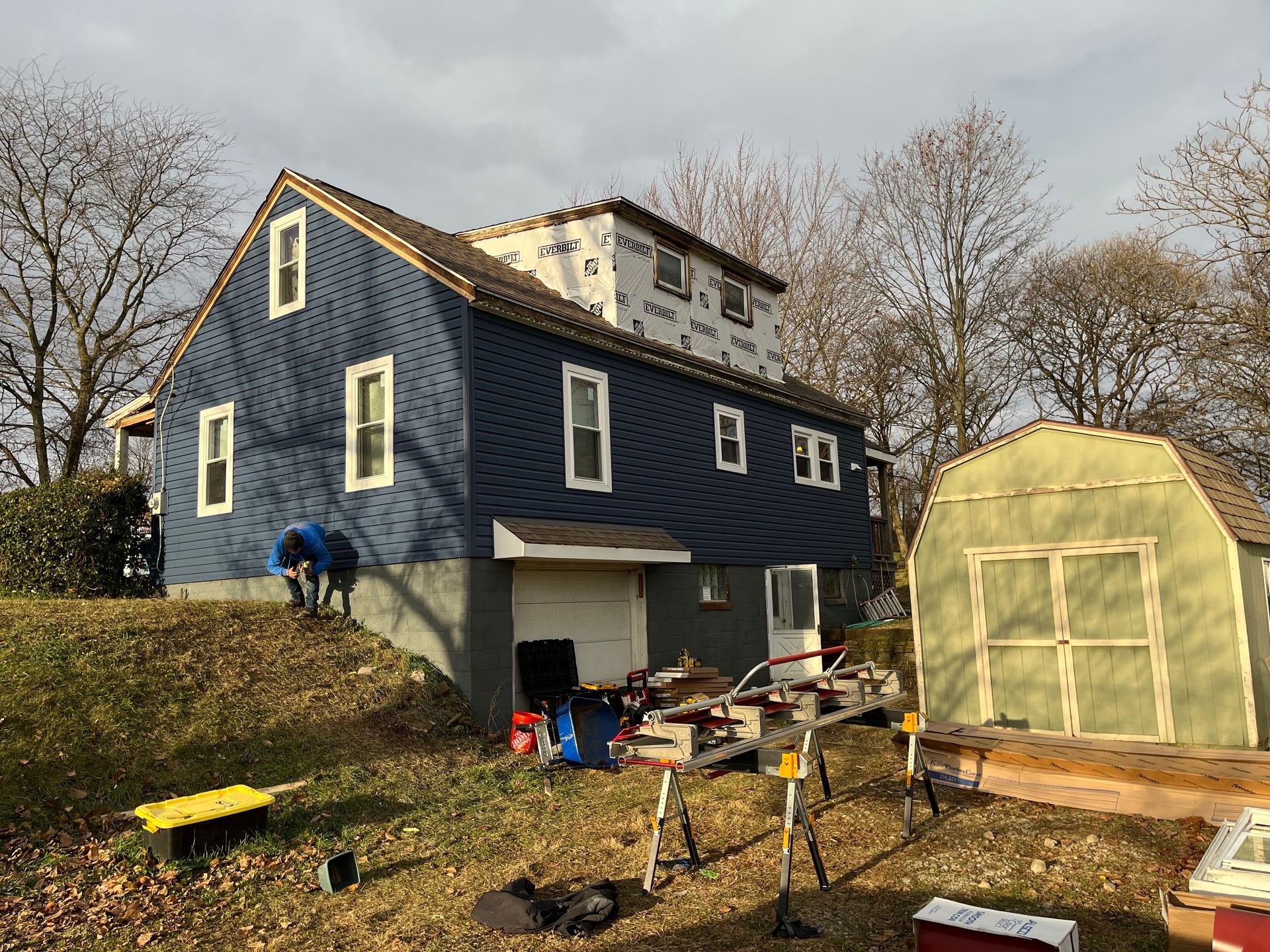 A blue house is being remodeled with a greenhouse in the background.