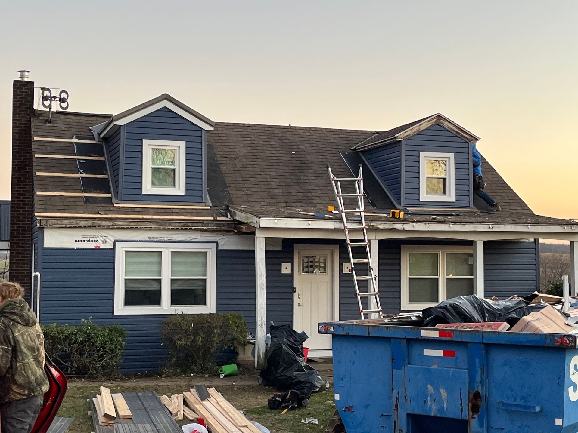 A blue dumpster is in front of a house that is being remodeled.