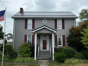A gray house with red shutters and an american flag in front of it