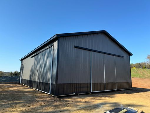 A large metal barn is sitting in the middle of a dirt field.