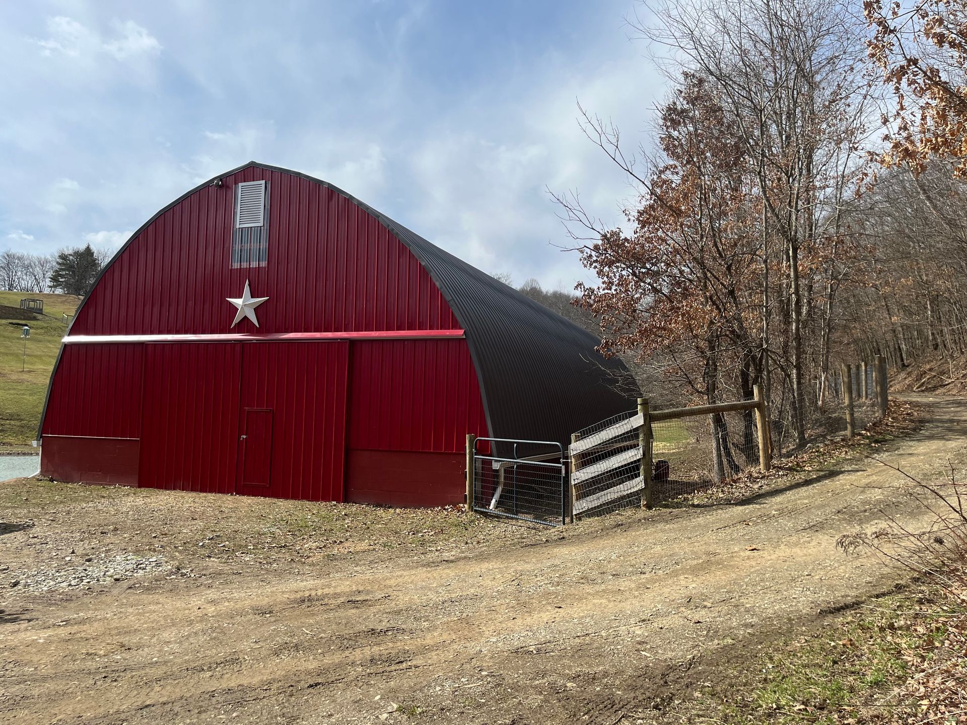 A large red barn with a star on the side is sitting on top of a dirt road.