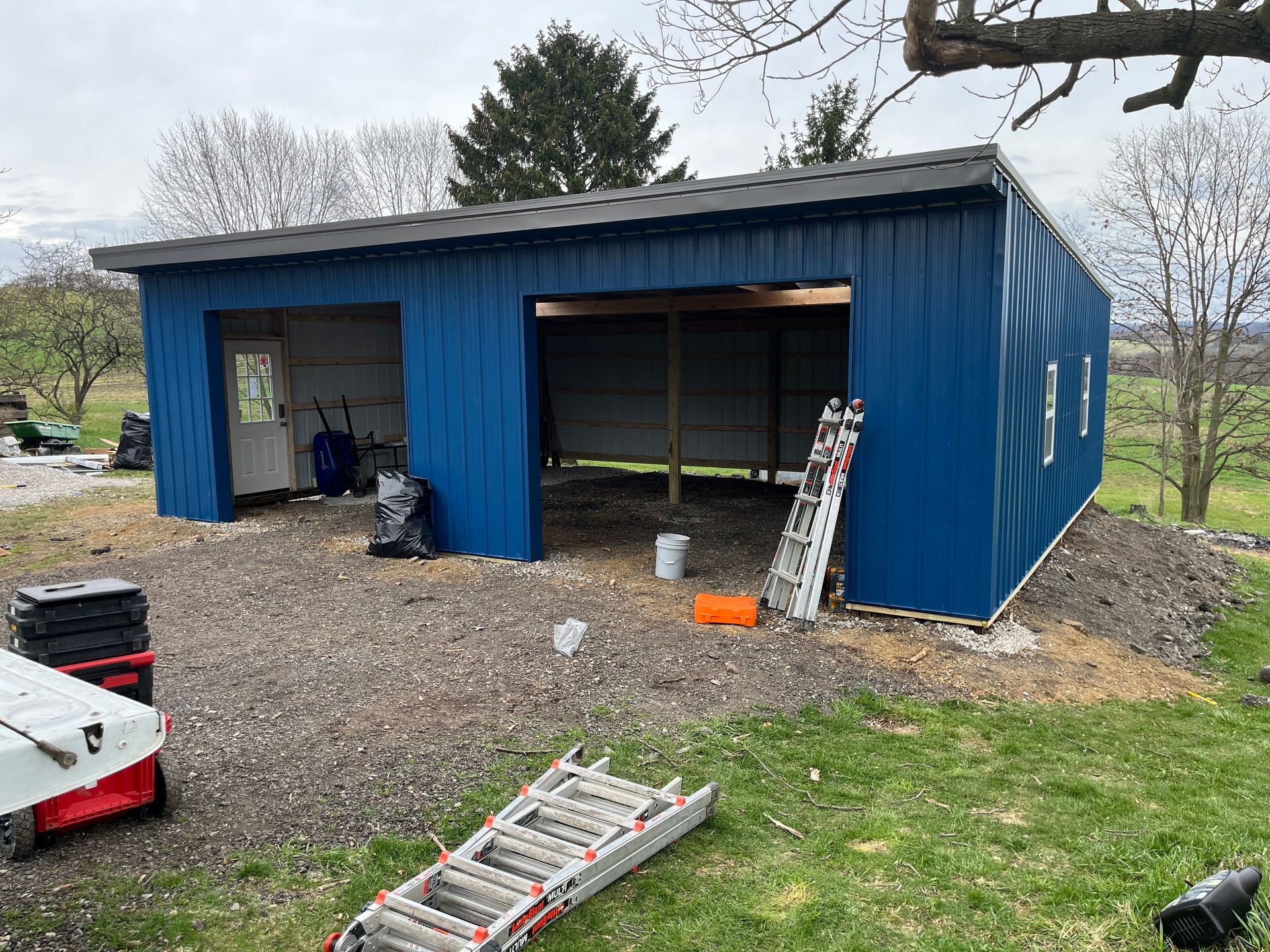 A blue metal garage is being built in a grassy field.