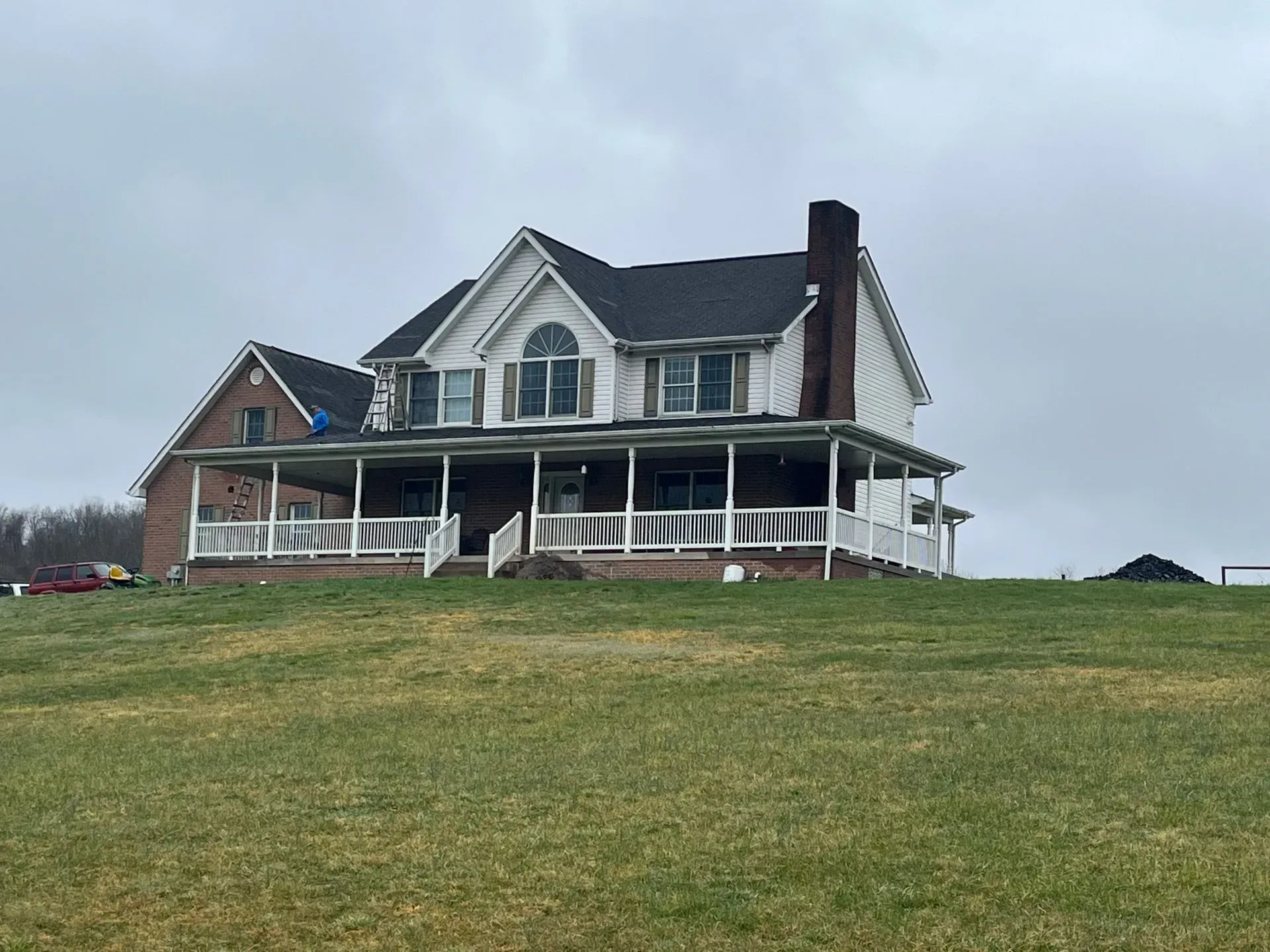 A large house with a porch is sitting on top of a grassy hill.