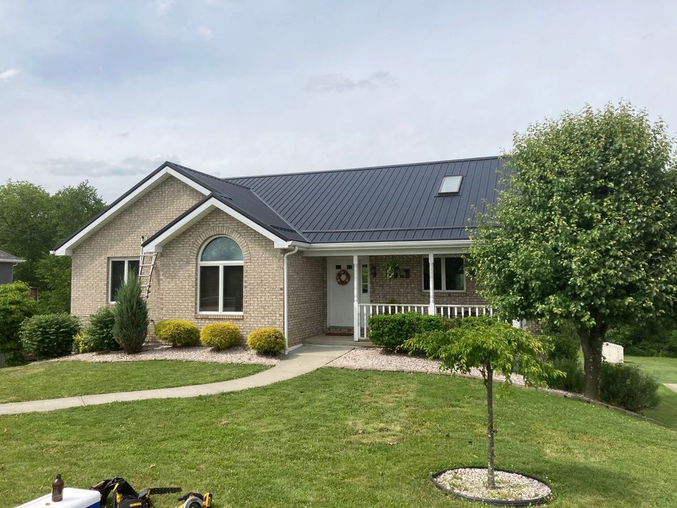 A brick house with a black roof and a large lawn in front of it.