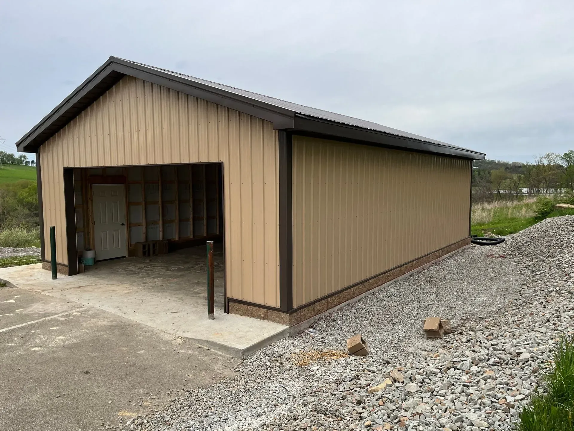 Tan metal garage with open bay and gravel border.