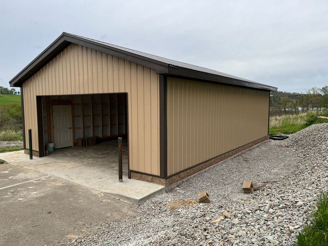A tan metal garage with a brown roof is sitting on top of a gravel lot.