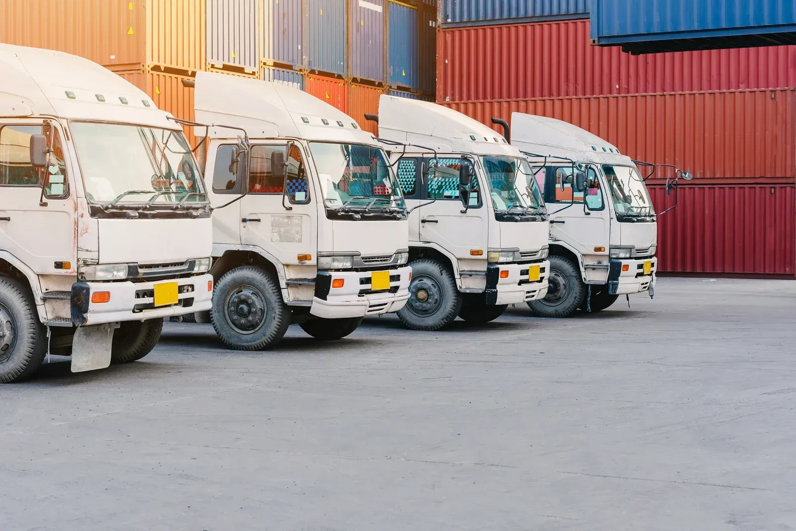 White trucks parked in front of shipping containers at a port.