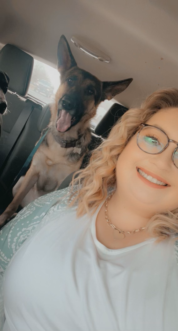 A woman is sitting in the back seat of a car with two dogs.