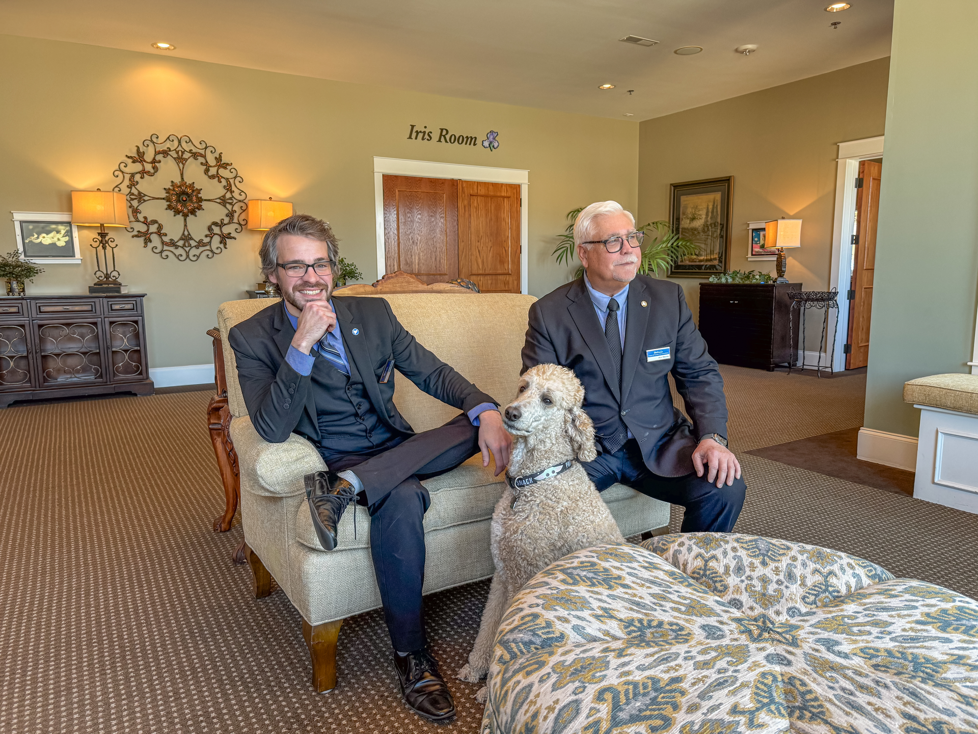 Two men are sitting on a couch with a dog.
