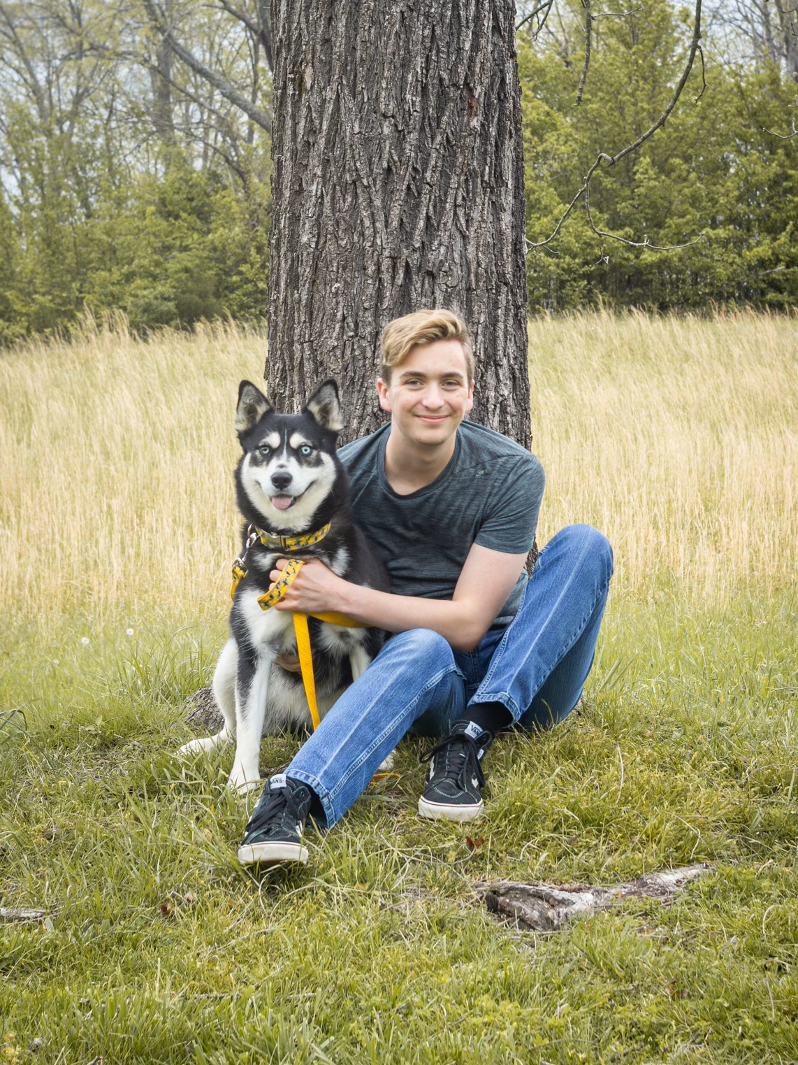 A young man is sitting in the grass with a dog.