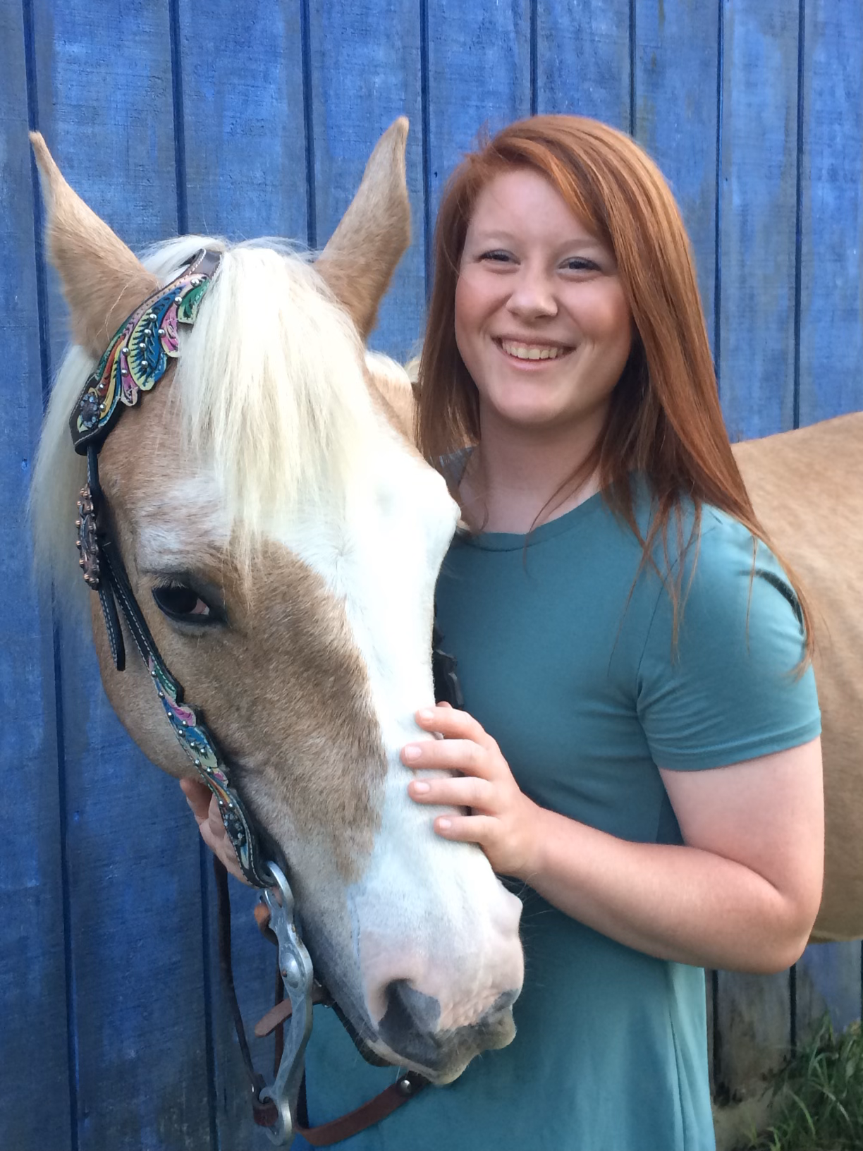 A woman is holding a brown and white horse in front of a blue fence.