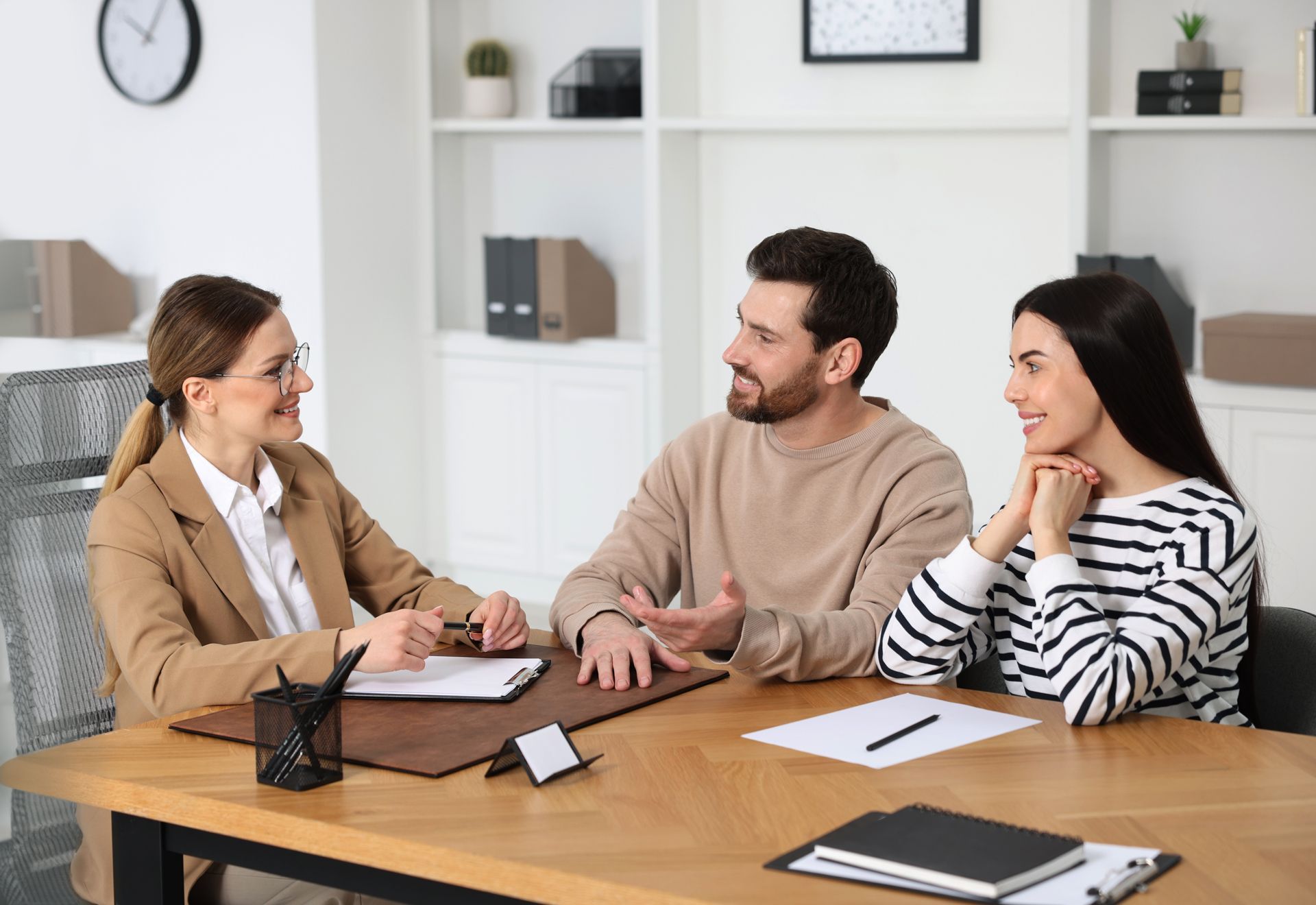 A woman in glasses advises a couple at a desk. 