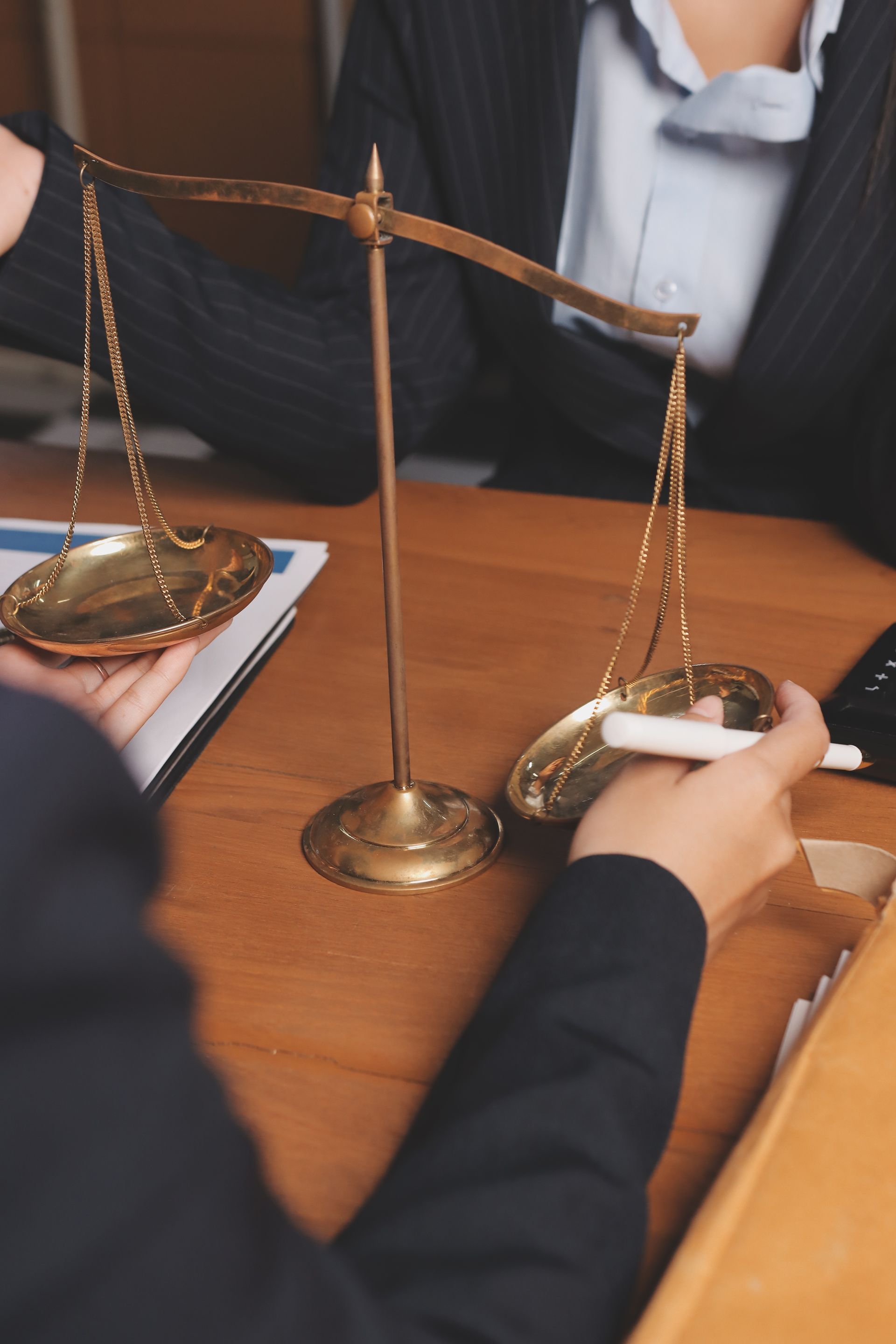 Scales of justice held by people in suits, weighing on wooden desk.