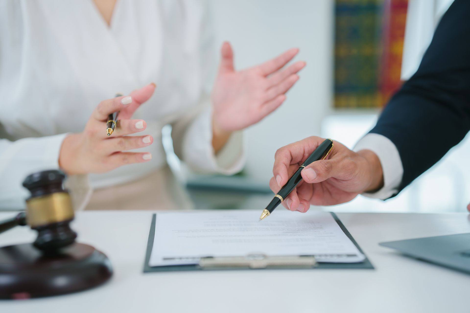 Person signing legal document with a pen, another person gesturing.