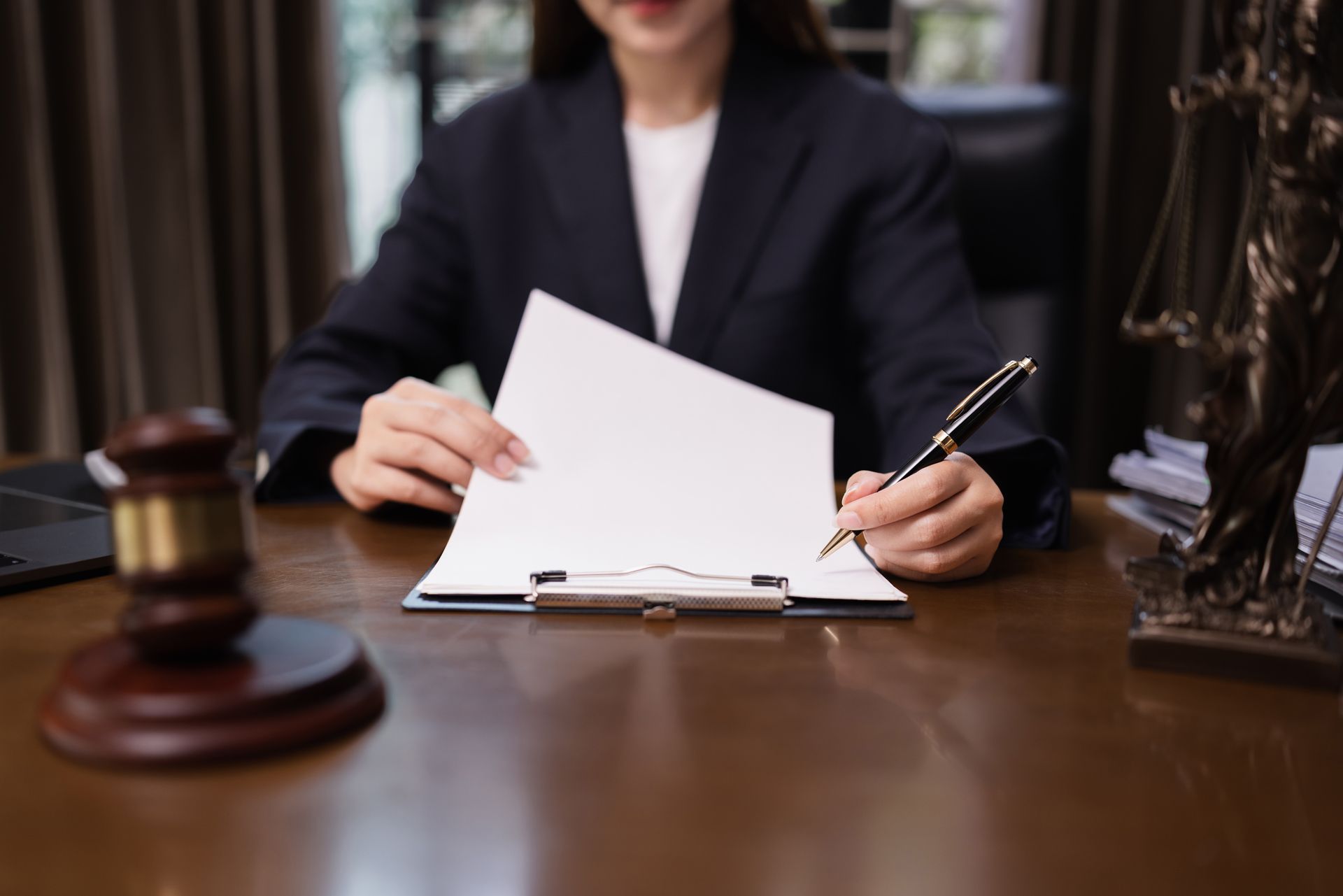 Lawyer in suit, writing on document at desk, with gavel and statue of justice.