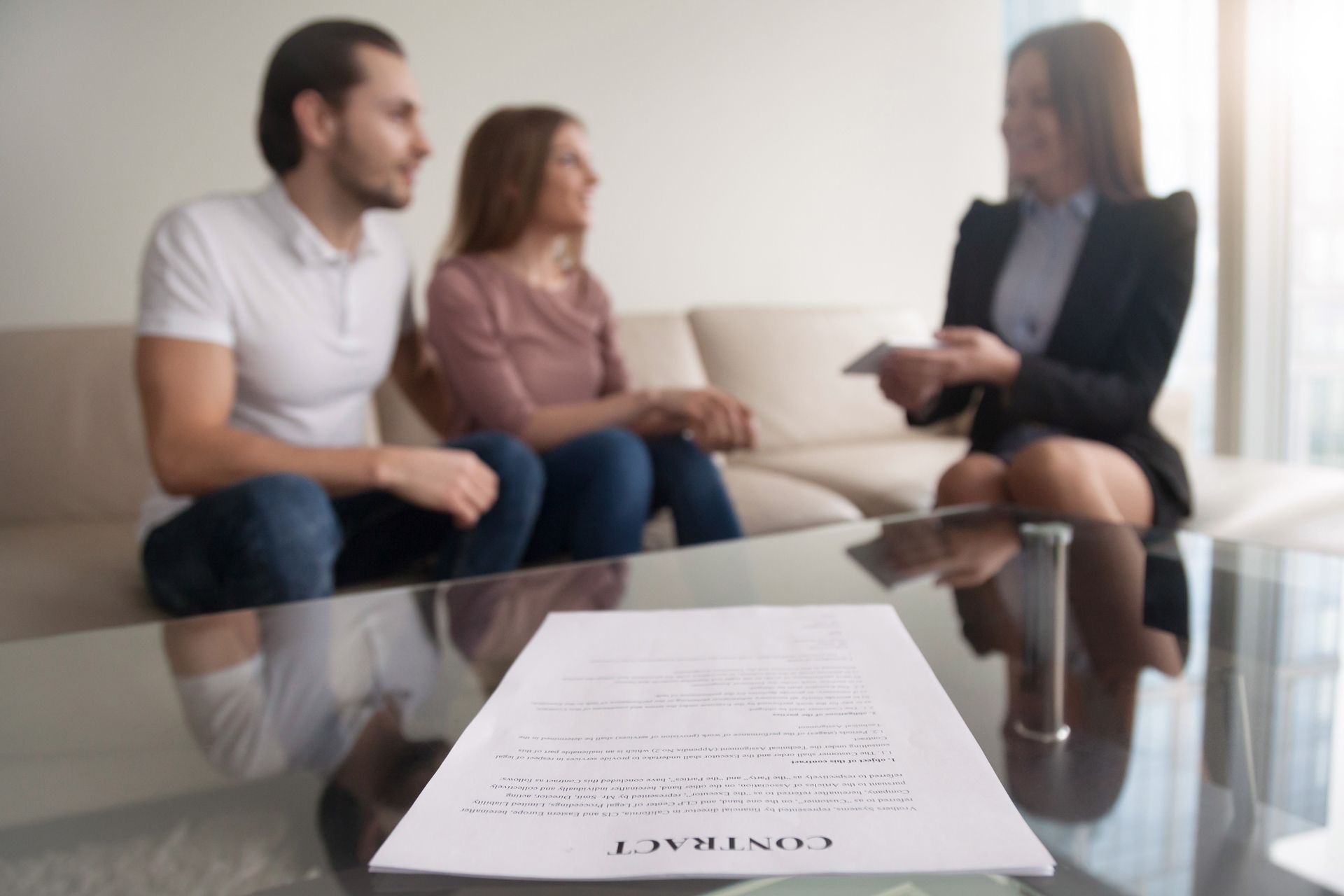 Contract on table with blurred couple on couch and person in blazer holding paperwork.
