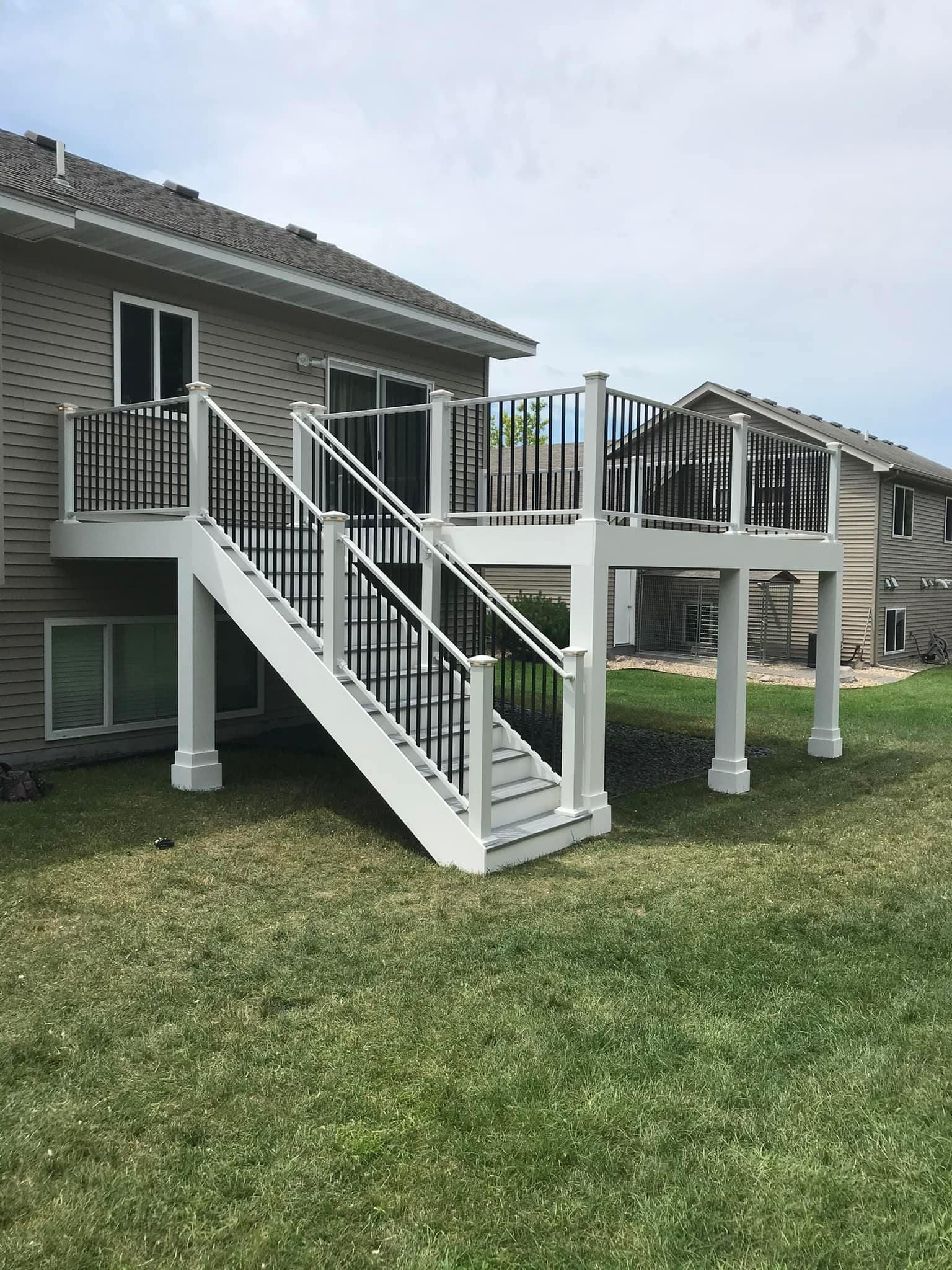 A white deck with stairs leading up to it is in the backyard of a house.
