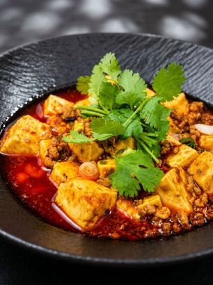 Curry tofu in a black bowl, topped with cilantro and served in a rich red sauce
