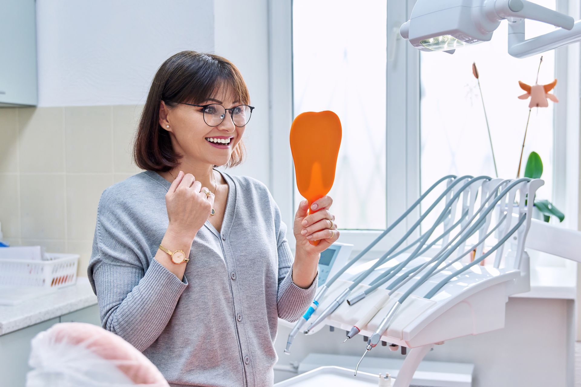 Woman at dentist smiling in hand mirror | dental implants Lynnwood WA