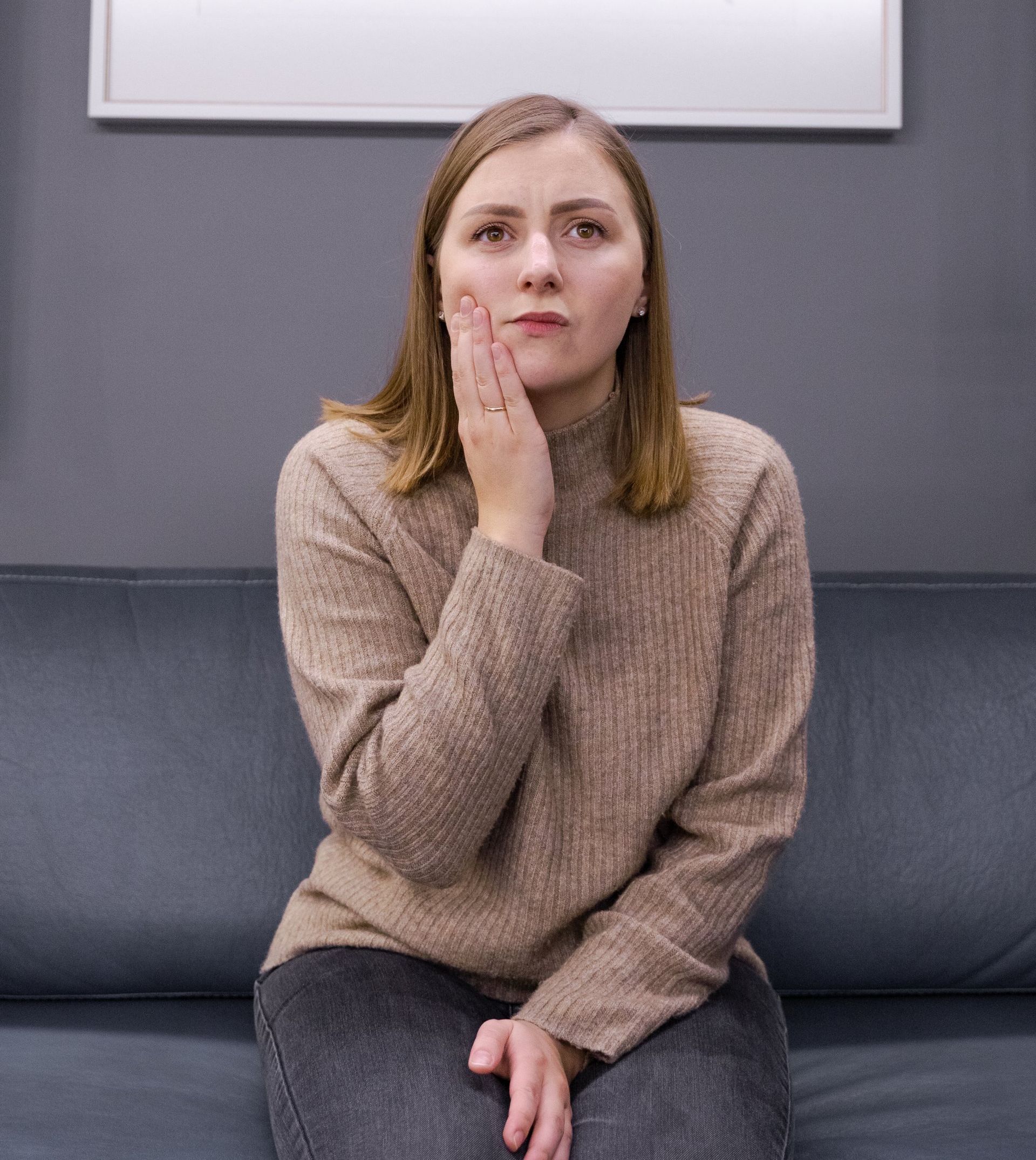 A woman is sitting on a couch with her hand on her face.