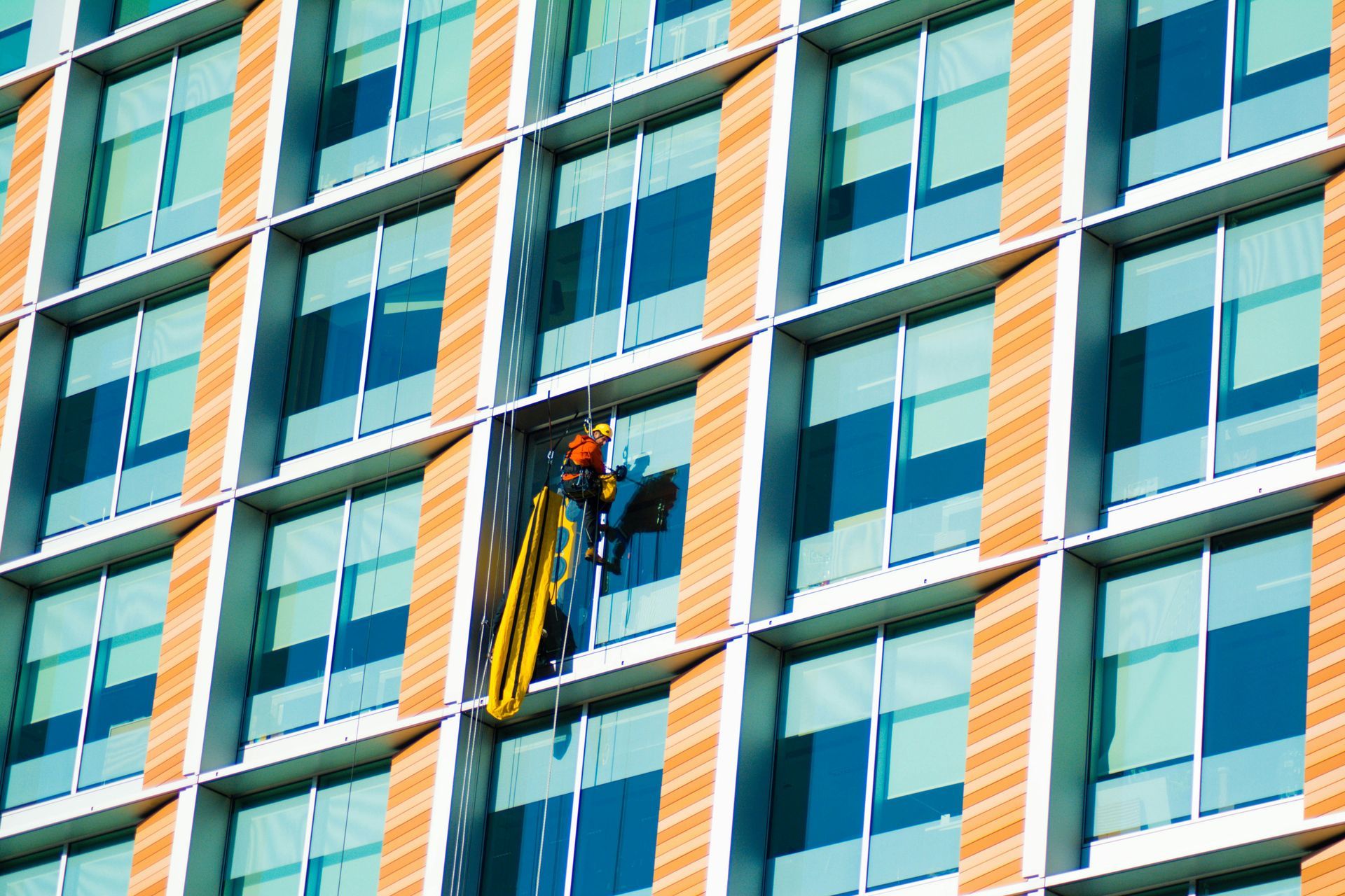 Worker suspended on a lift cleaning windows of a modern glass high-rise building