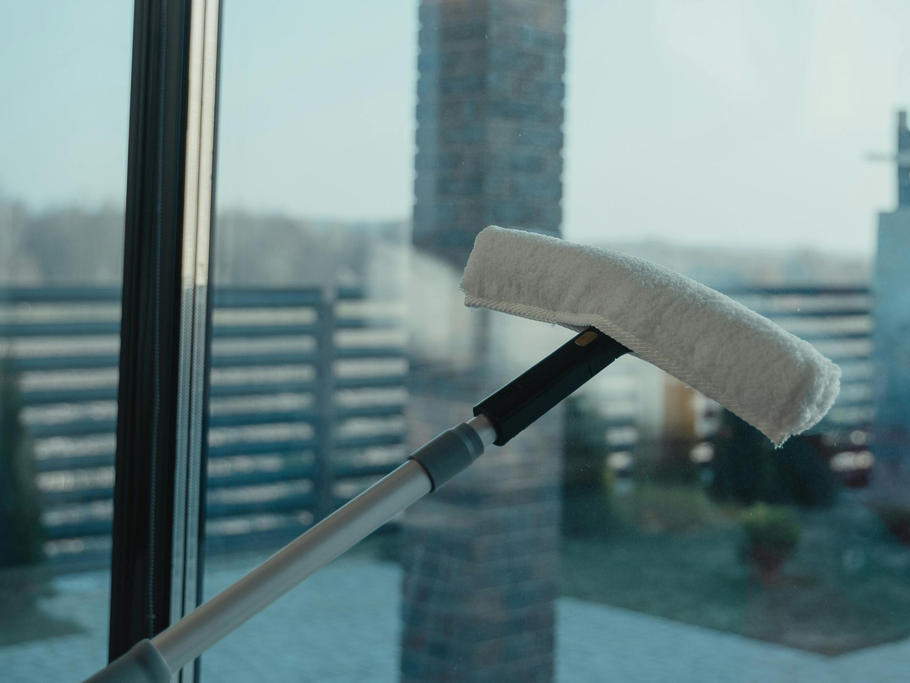 White window squeegee on a pole beside a window, with city buildings blurred in the background