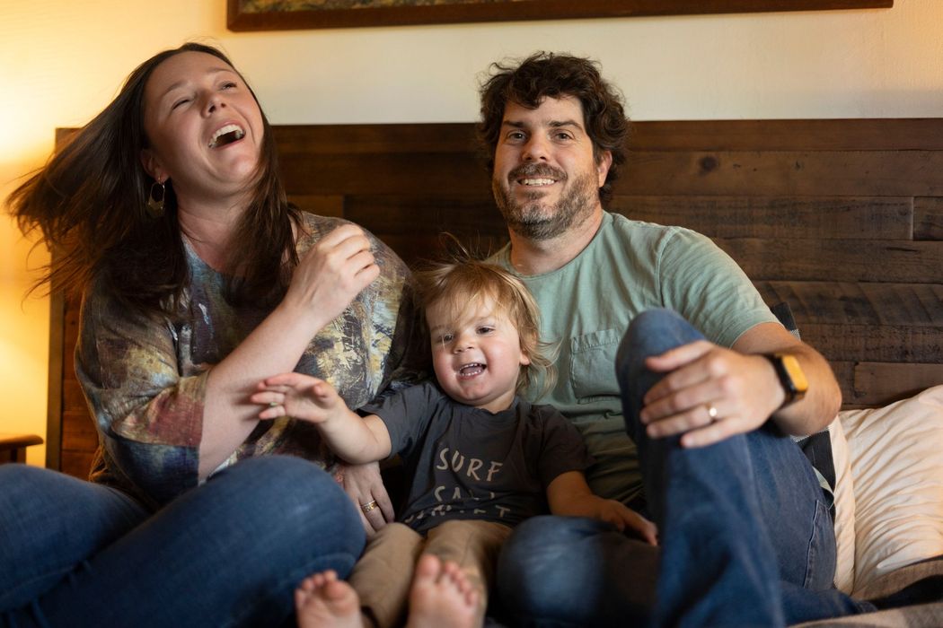 A man and woman are sitting on a bed with a child.