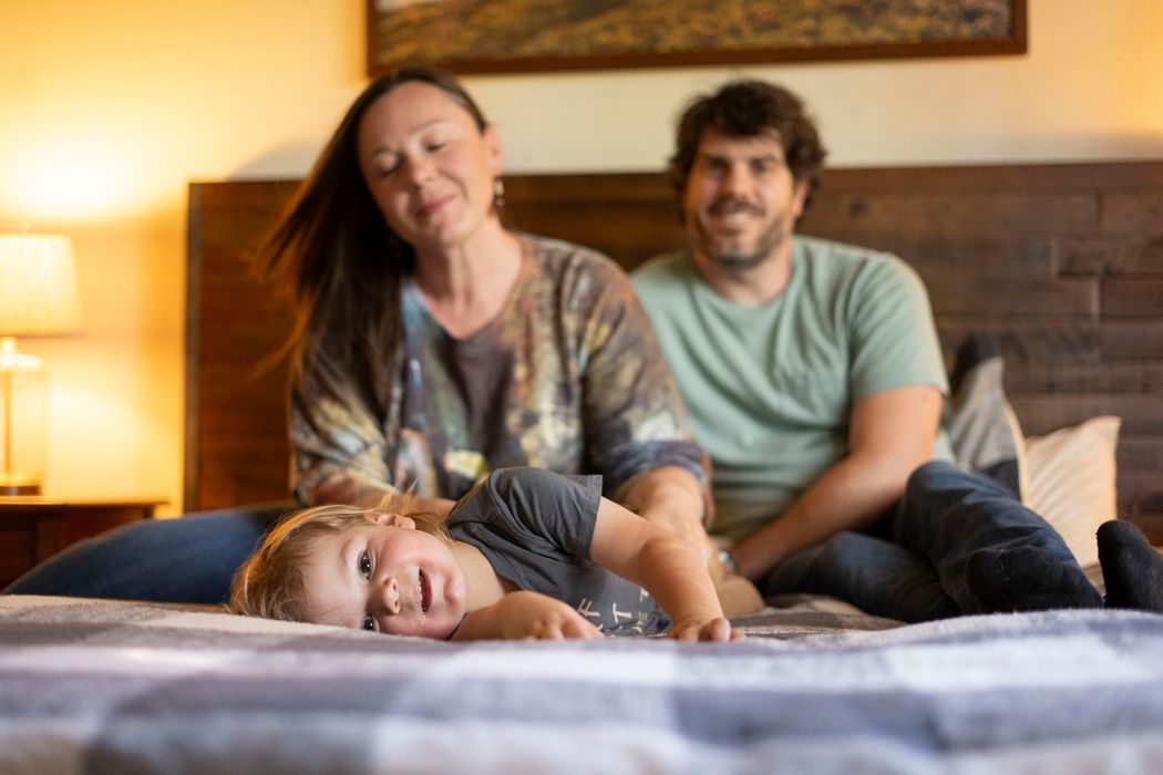 A family is sitting on a bed with a child laying on the bed.