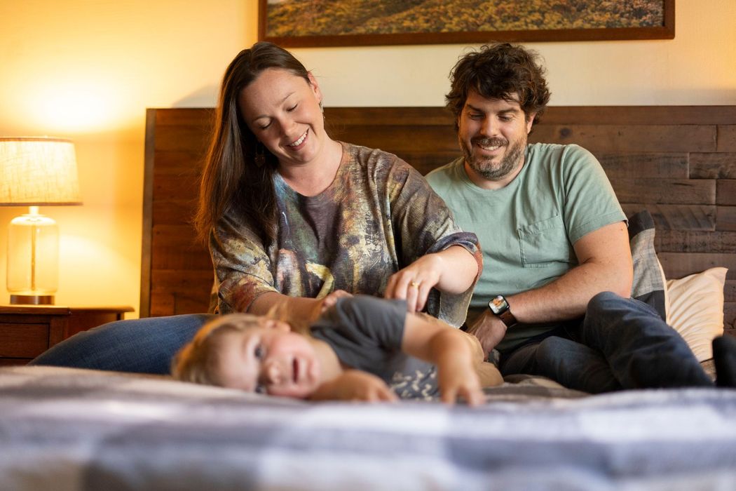 A family is sitting on a bed playing with a child.