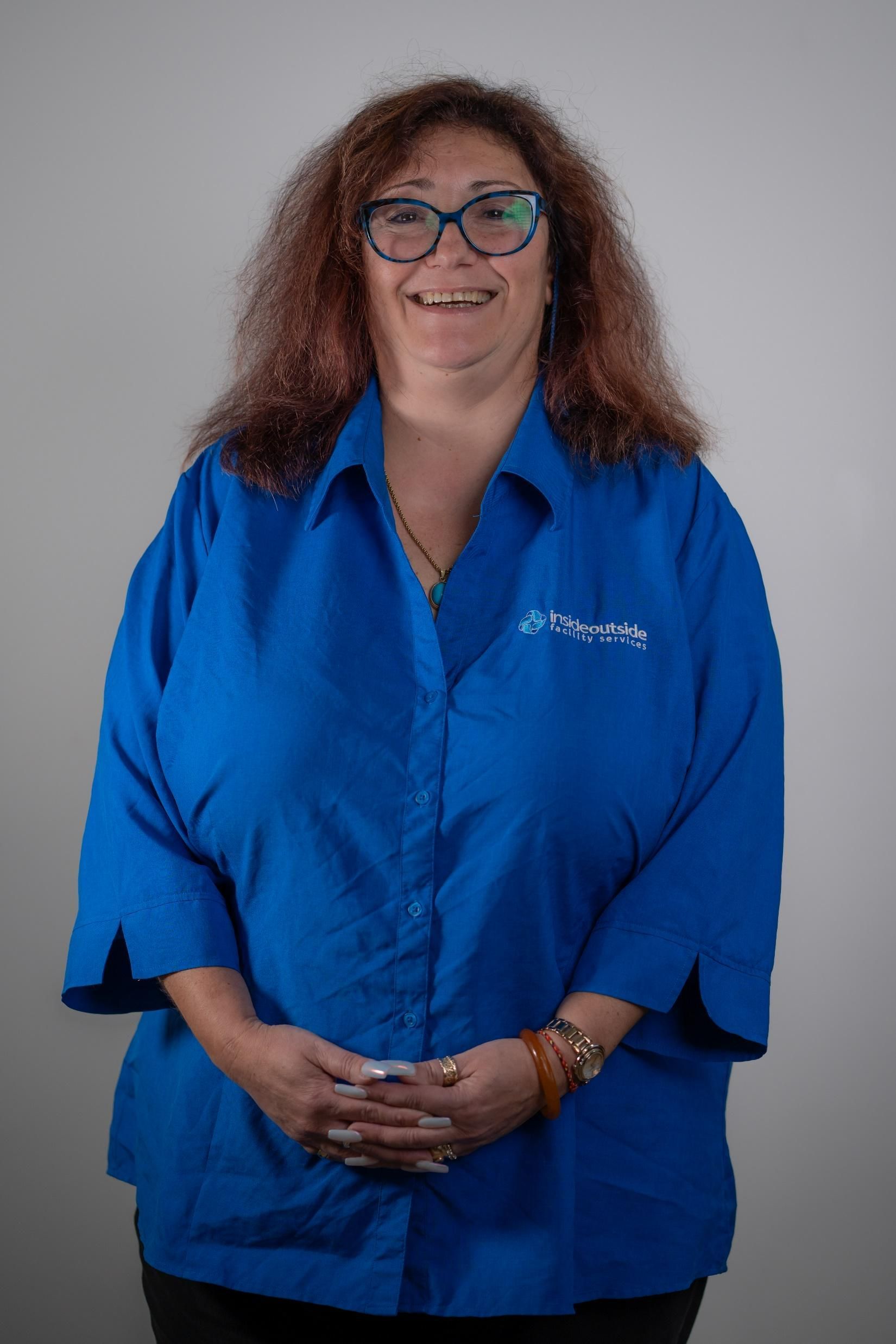 A woman wearing glasses and a blue shirt is smiling.