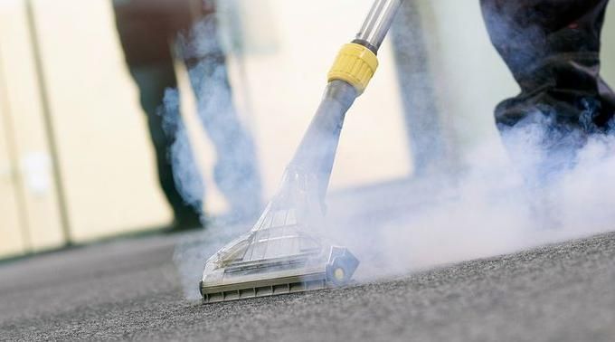A person is cleaning a carpet with a steam cleaner.