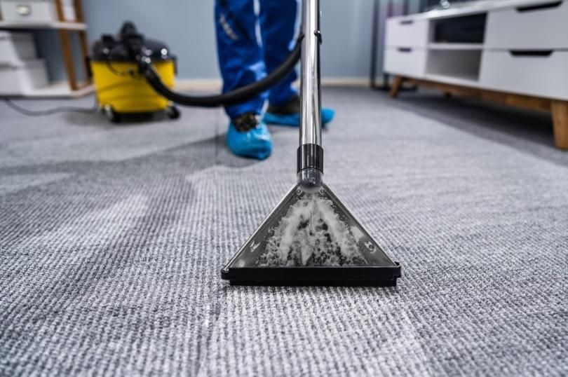 A person is cleaning a carpet with a vacuum cleaner.