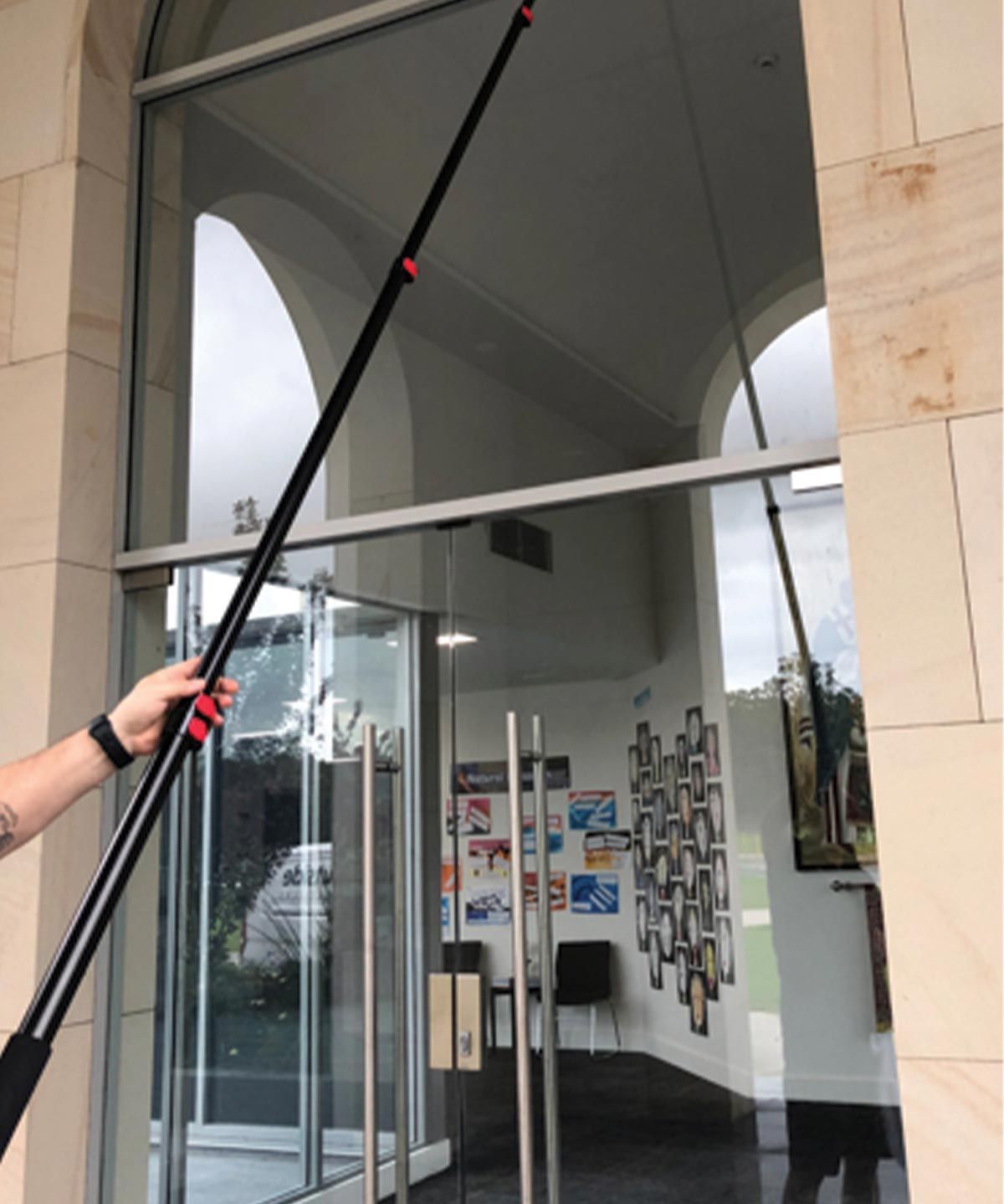 A person cleaning a glass door with a long pole