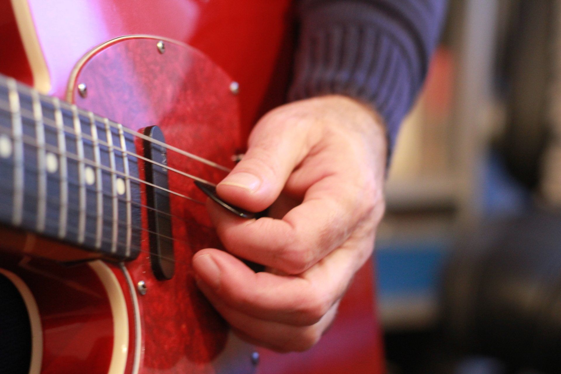 A guitarist's picking hand playing a red electric guitar