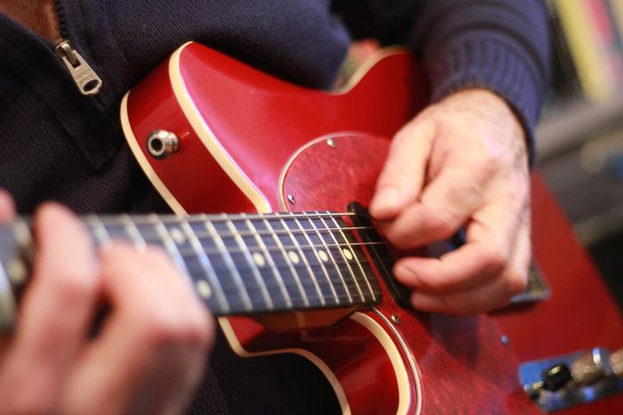 A guitarists' hands playing a red electric guitar