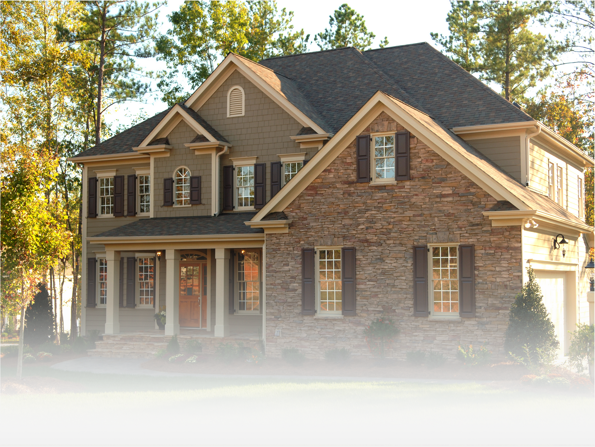 A large, two-story house with a stone facade, dark shutters, and a shingled roof, surrounded by trees.