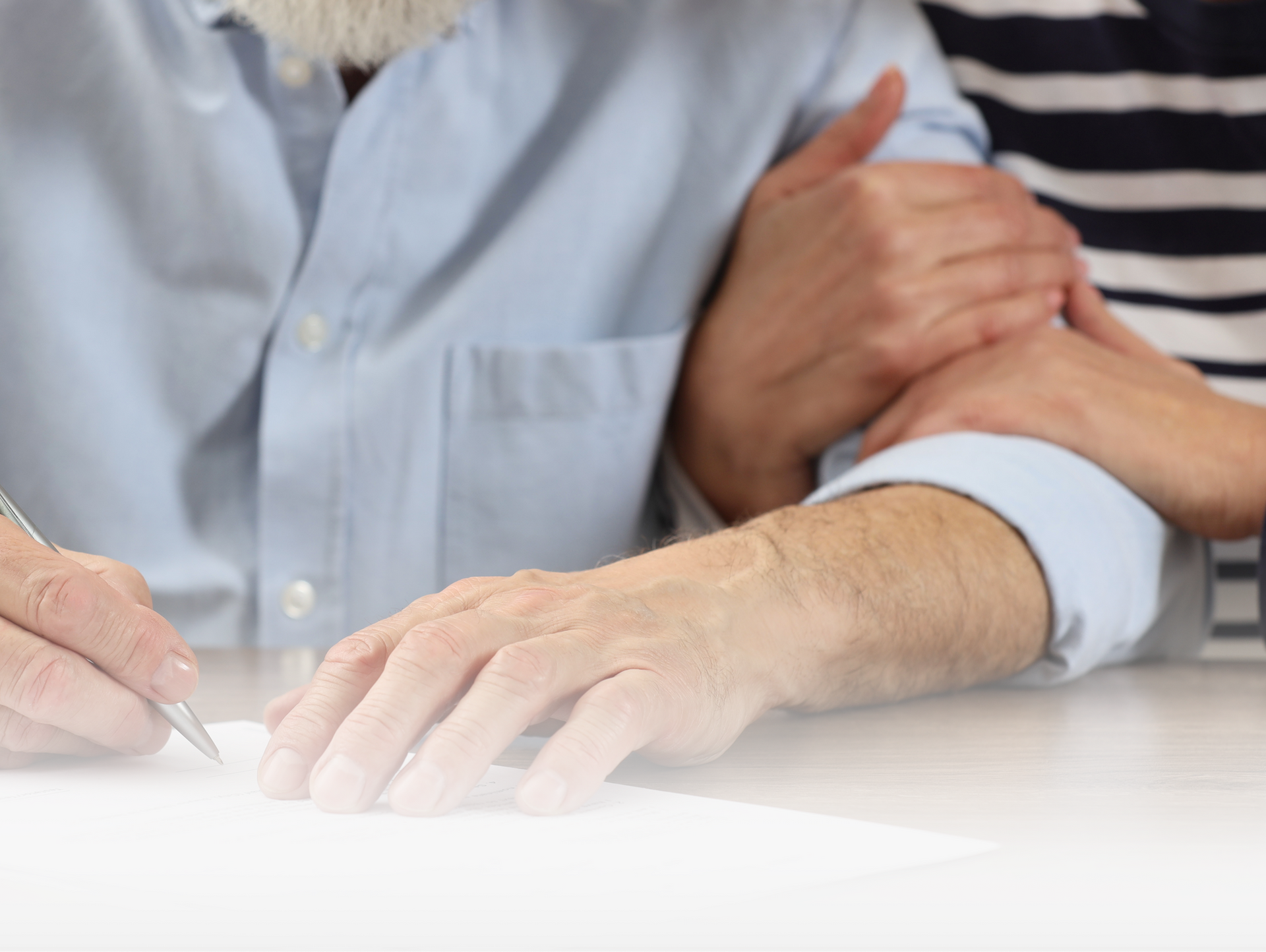 A person signing a document while someone else places a hand supportively on their shoulder.
