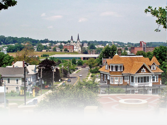 An elevated view of a residential town featuring historic homes, leafy trees, and a distant church with twin steeples.