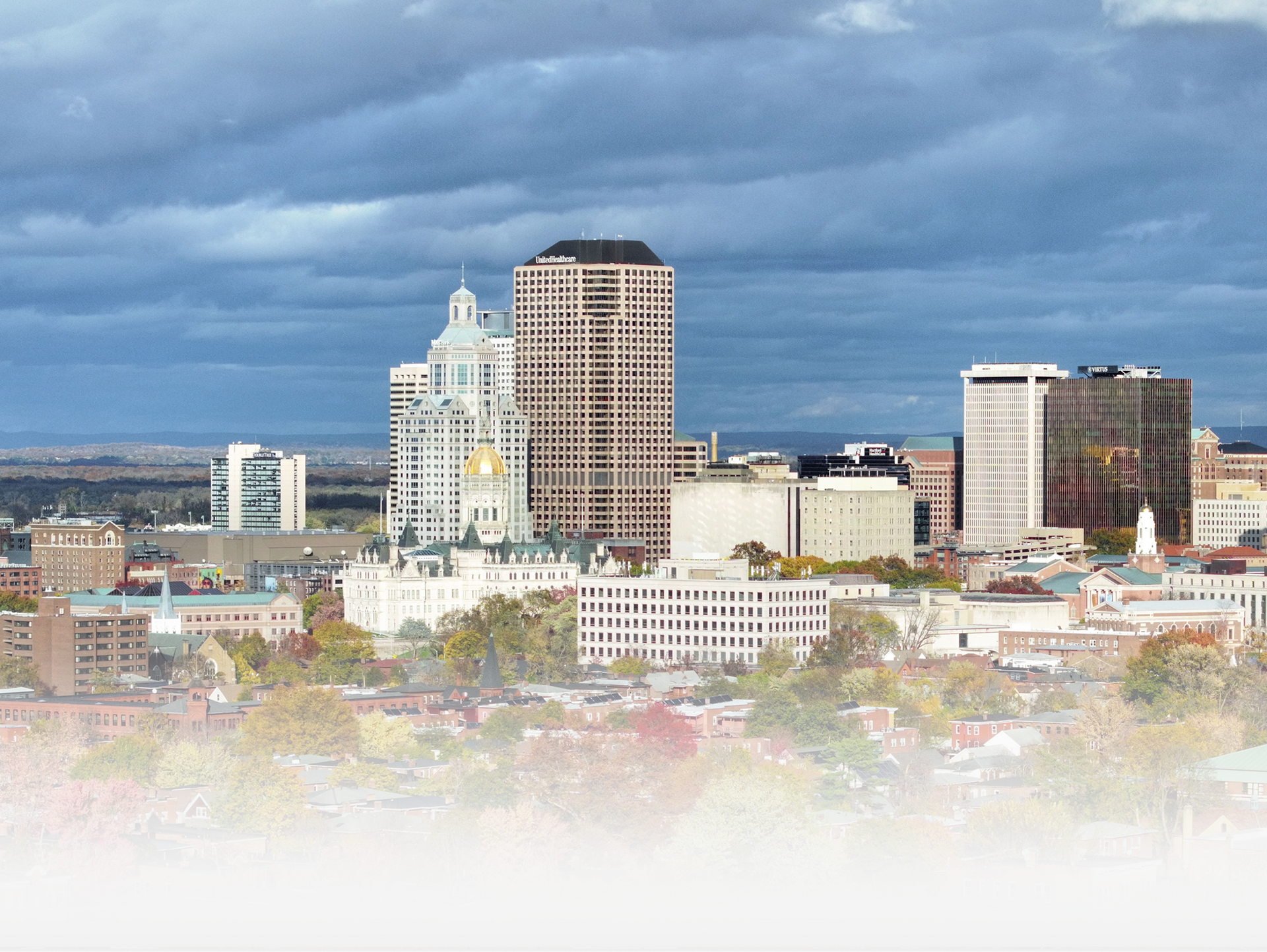 A scenic, elevated view of the Syracuse, New York skyline featuring prominent buildings under a cloudy blue sky.