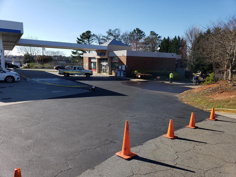 Gas station with newly paved asphalt, orange cones, and a building on a sunny day.