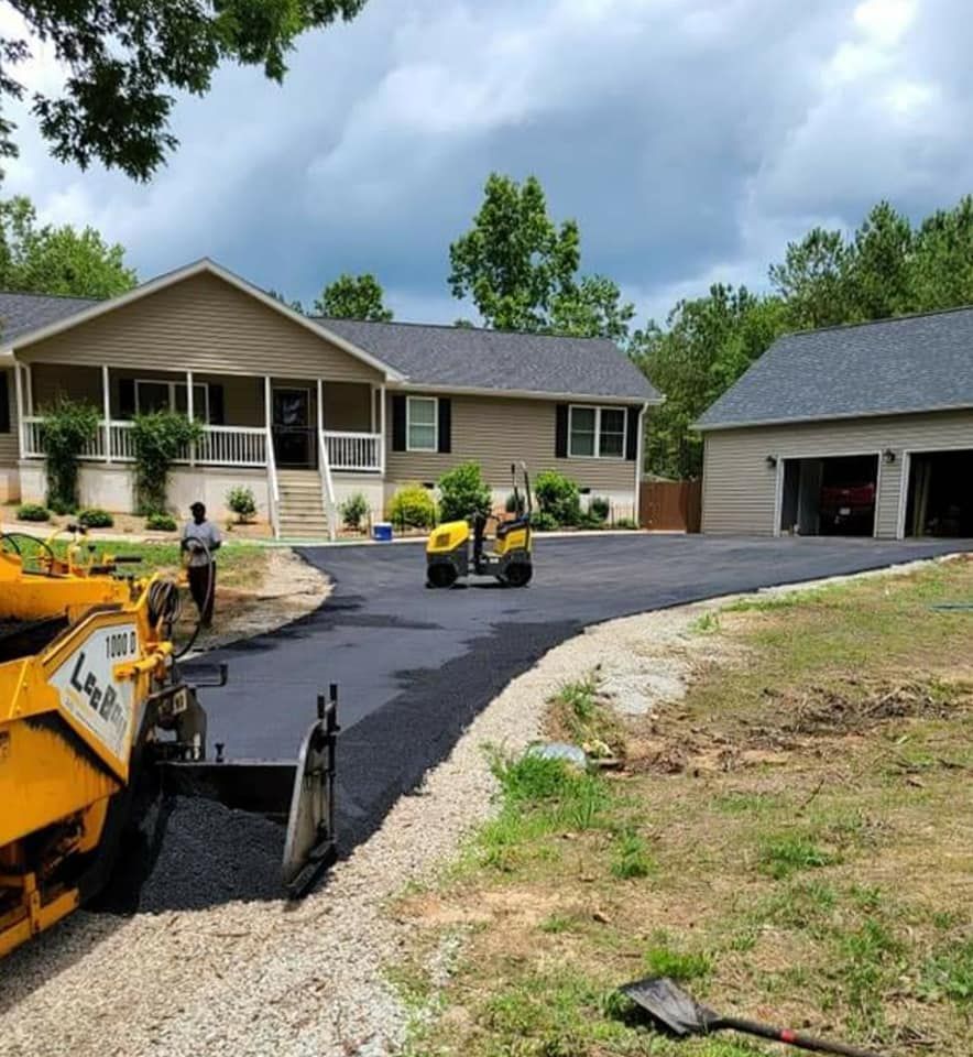 Asphalt driveway being paved at a house and detached garage. Construction workers operate machinery in setting.