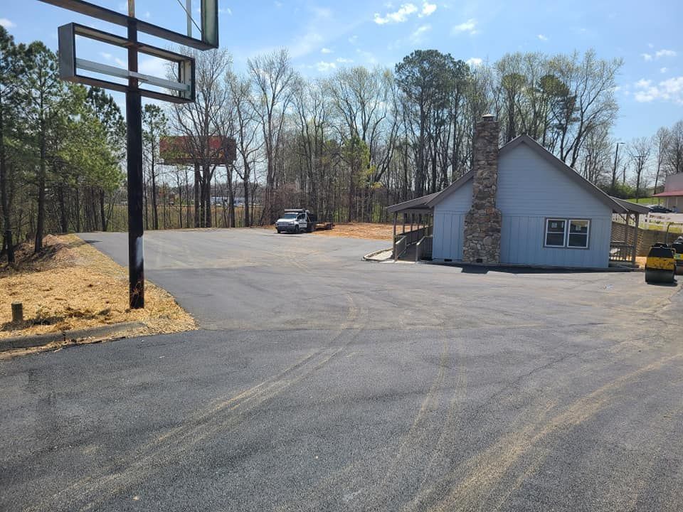 A paved parking lot with a truck, sign frame, and a small blue building with a stone chimney.