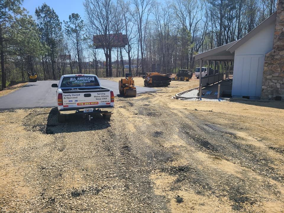 Construction site with a white pickup truck, paving equipment, and building.