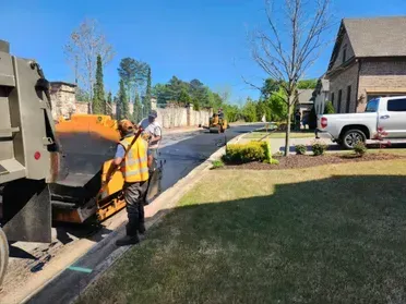 Asphalt paving on residential street with workers, machinery, and a truck.