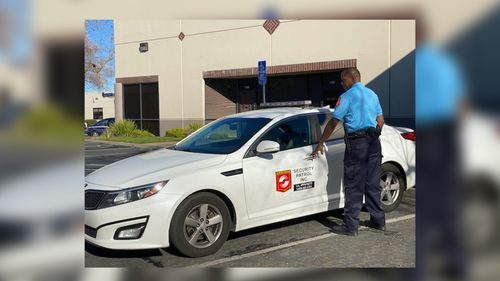Security guard in blue uniform opening the door of a white security car with logo on the side in a parking lot. Elk Grove, CA — Airborne Security Patrol, Inc.