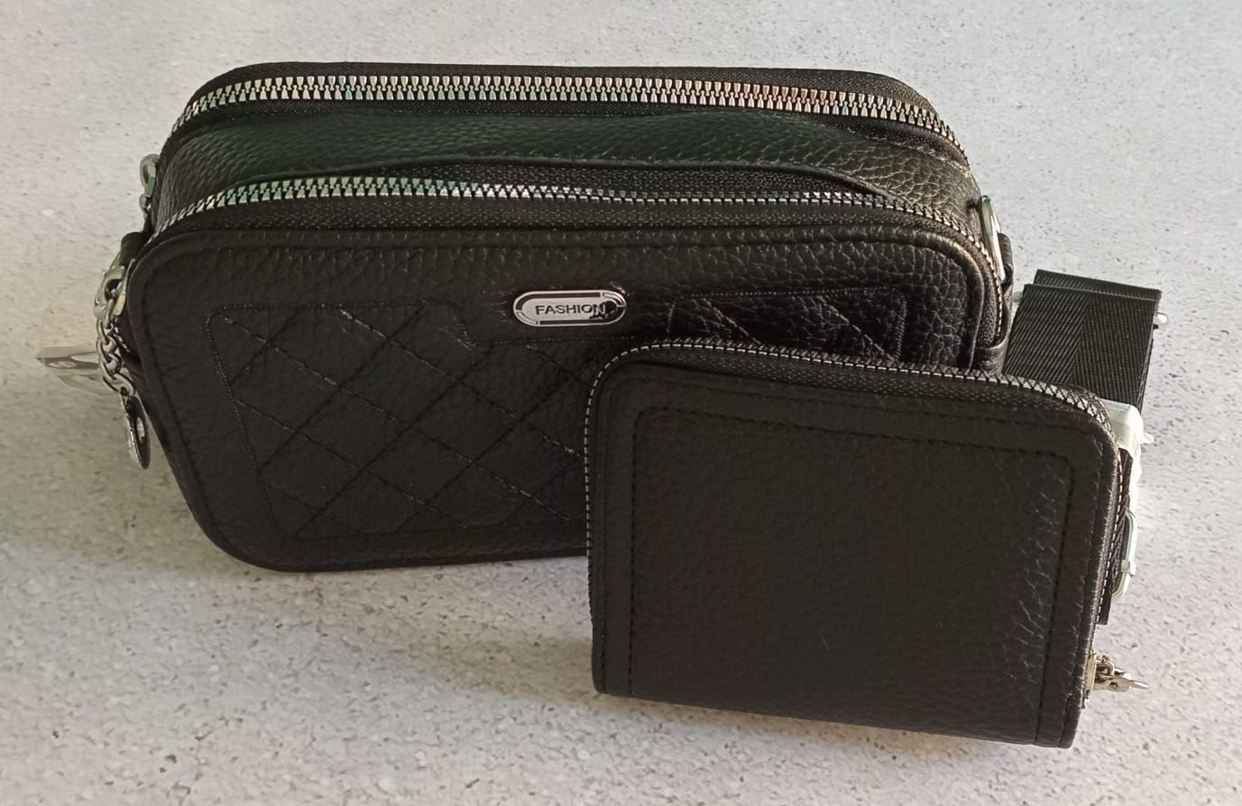 Bolso bandolera acolchado negro y cartera a juego sobre una superficie gris claro.