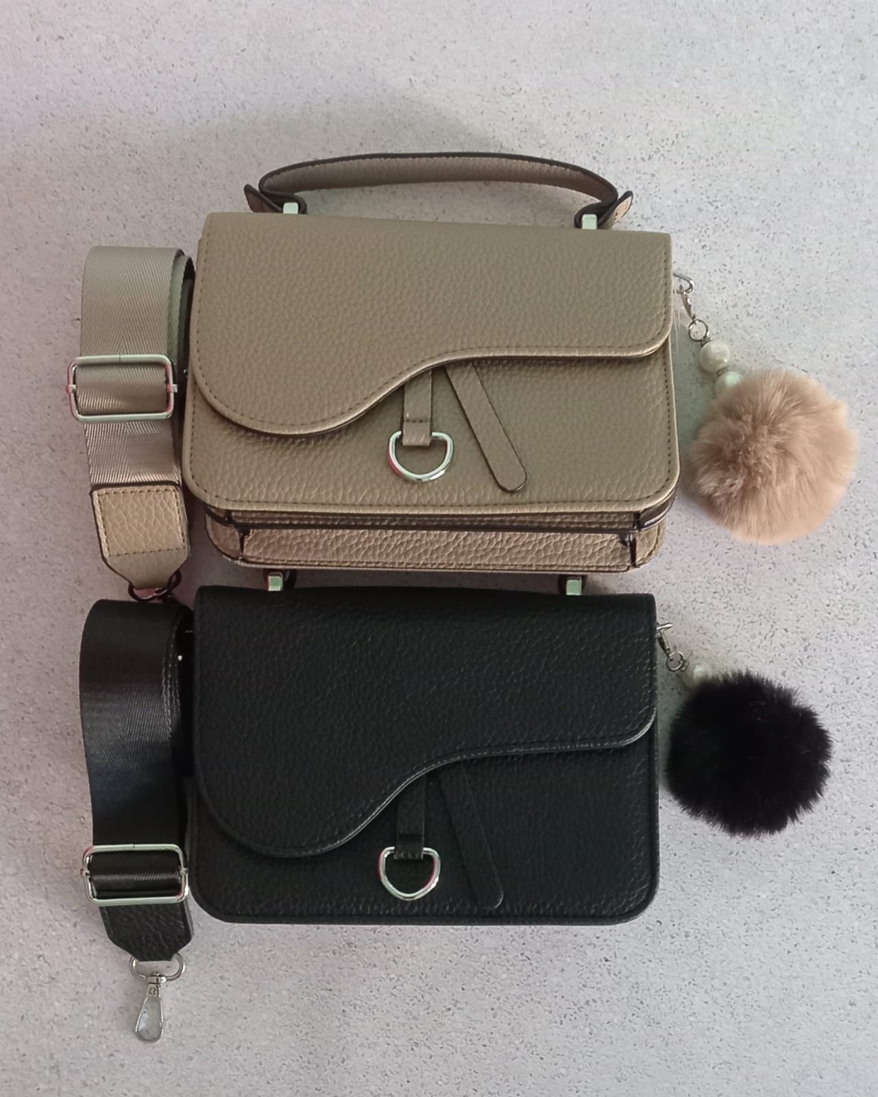 Dos bolsos con forma de silla de montar, en color tostado y negro, con correas para los hombros y adornos de pompones.