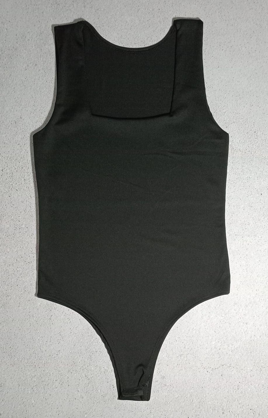 Body negro sin mangas con escote cuadrado, dispuesto plano sobre una superficie texturizada.