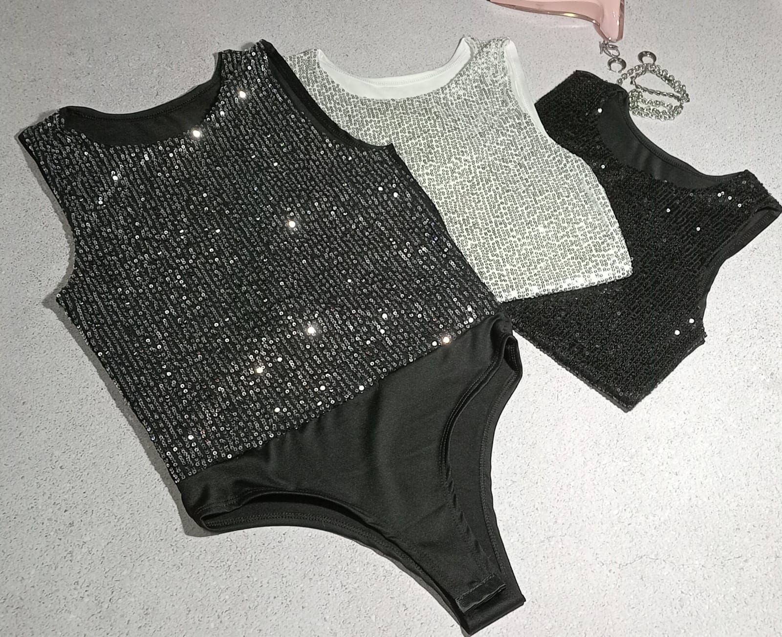 Tres monos sin mangas con lentejuelas en negro, plata y gris.